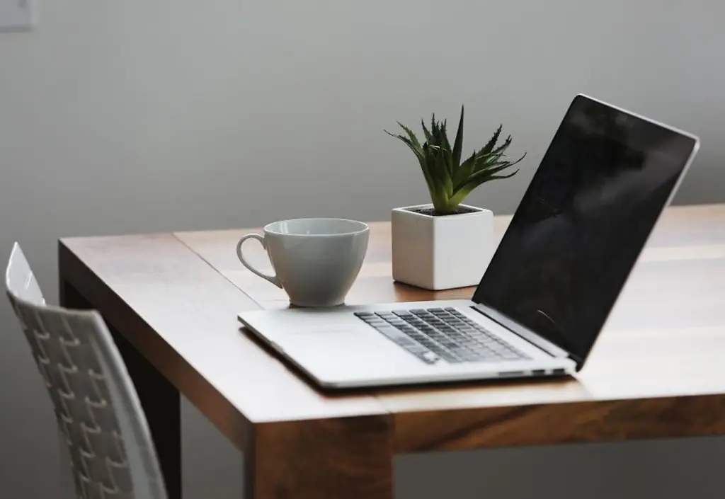 A breakfast bowl, a notebook and a laptop showing a video call, set out on a kitchen table